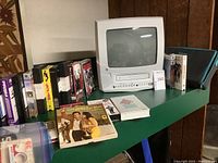 GE white swiveling VHS player with TV and assorted VHS tapes on green table
