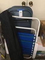 Full view of four stacked blue metal folding chairs, one folded blue and green striped beach chair, and one folded chair in a black canvas bag.