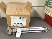 Hitachi CP-X328WT projector box with Targus tripod placed in front, showing the lot items together.