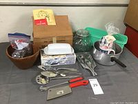 Photo showing assortment of kitchen tools including butter dish, cookie cutters, green pan, glass bowl, saucepan, and various utensils with red handles