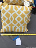 Square yellow and white geometric patterned Solarium decorative cushion with measuring tape showing approx. 18 inches