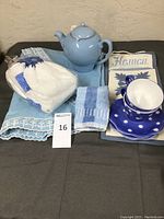 Lot displayed on dark surface showing blue teapot, two blue and white polka dot tea cups and saucers, folded tablecloth and hand towels.