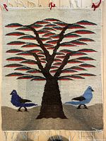 Front view of the woven textile showing the tree of life motif with two birds on a cream background and fringed edges