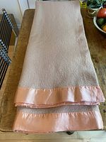 Folded wool blanket showing oatmeal color and melon satin binding.