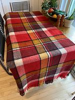 Full view of wool blanket spread on a metal frame showing large red plaid pattern with cream, mustard, and black checks.