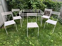 Full set of white wrought iron patio table and five matching chairs on grass outdoors