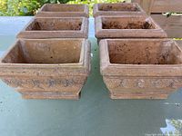 Top view of the six matching rectangular clay garden pots arranged in two rows on a table outdoors. Each pot has textured raised swirly motifs around sides.