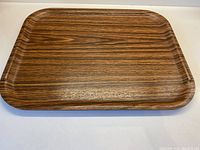 Top-down photo showing rectangular synthetic teak tray with rounded corners and wood grain pattern.
