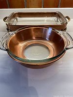 View showing both the round and rectangular glass casserole dishes within their copper and brass framed bases with handles.
