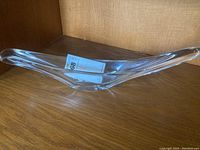 Front angle view of the clear elongated boomerang-shaped art glass bowl on wooden surface