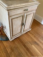 View of front and side of the cabinet showing distressed wood finish, drawer, locking double doors, and metal handles.