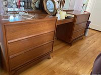 Photo showing two matching wooden dressers with mid-century modern design, three drawers each, placed side by side with various decorative items on top.