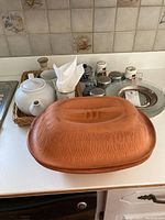 View of Scheurich Schlemmeropf Dutch oven, ceramic teapot, mugs, salt and pepper shakers, and glass plates on kitchen counter.