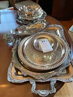 Full set of silver-plated serveware including trays, plates, and tongs arranged on a wooden surface.