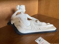 Full side view showing reclining Venus figure resting on a dark base with smooth white finish and detailed draped cloth