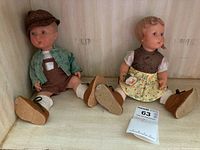 Two vintage German Hummel dolls, a boy and a girl, seated with visible full view for condition and attire.