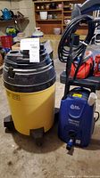 Photo shows a yellow and black Shop Vac wet/dry vacuum and a blue Blue Clean Speedy Wash electric pressure washer side by side in a garage setting.