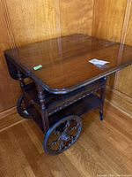 Overall view of wooden tea cart showing drop leaf sides and large spoked wheels.