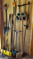 Full view of yard tools hanging on wall including shovels, aerator, folding hand cart.