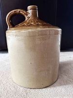 Front view of two-tone stoneware crock showing beige body, brown glazed top, handle and spout