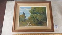 Full view of framed oil on board landscape painting depicting a dirt path with trees and blue sky, with the scale shown by tape measure.