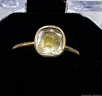 Close-up of ring front view showing cushion-shaped canary slice cut diamond in gold-plated bezel against black velvet