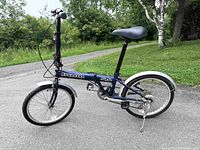 Full left-side view of folded-out bicycle showing frame, wheels, saddle, handlebars and kickstand on pavement
