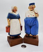 Front view of hand carved and painted Dutch couple figurines on wooden bases, showing detailed carving and coloring with a coin for size reference.