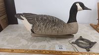 Side view of life-size goose decoy resting on white table with measuring tape indicating approximately 24 inches length.