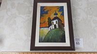 Framed oil painting showing a small church with a blue onion dome on a green hill against a dramatic sky.