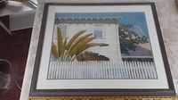 Framed pastel painting showing entire artwork including white picket fence, plants and white houses under blue sky.