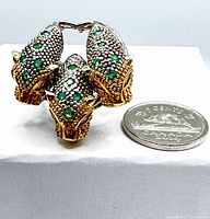 Front view of the three tiger heads silver ring with green chrome diopside stones and gold accents beside a Canadian quarter for scale.