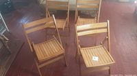 Four solid maple folding chairs on a wood floor, all unfolded and standing upright.