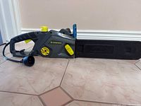 Side view of the Yardworks electric chainsaw showing body, handle, yellow adjustment controls and power cord.