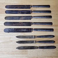 Top view of all nine knives, showing handles and blades on wooden surface with visible signs of wear and scratches.