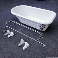 White clawfoot cast iron bathtub with worn exterior paint, two metal shower rods and four clawfoot feet arranged on ground