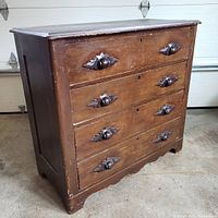 Front angled view of the dresser showing four drawers with carved wooden pulls and keyholes, surface wear visible.
