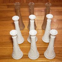 Photo showing 6 white milk glass bud vases in the front row, and 3 clear glass bud vases behind on a wood floor.