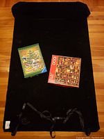 Photo of the rolled out black inflatable puzzle saver mat with two boxed jigsaw puzzles placed on top showing cover artwork of Christmas tree and vintage dollhouse scenes.