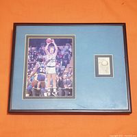 Framed photo showing Larry Bird shooting over Magic Johnson with unused James Naismith stamp mounted to the right on blue matting. Frame and matting visible.