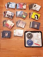 Photo showing multiple stacks of CDs, including jewel cases and some loose discs in a binder.
