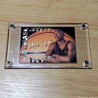 Michael Jordan retirement basketball card in clear plastic screw-down case laying on wood surface, showing front of card with holographic elements and printed autograph.