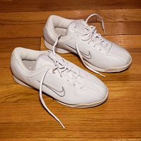 Pair of white Nike Air running shoes for women, size 8, showing side angle and top view on wooden floor.