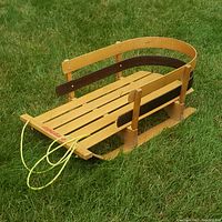 Wooden Torpedo sleigh shown on grass from an angled front side view, displaying the pull rope, slatted seating and side rails.