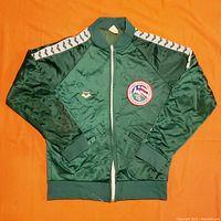 Full front view of dark green jacket with white shoulder stripes, front zipper, and two front pockets, laid flat on orange background.