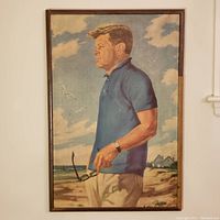 Full front view of framed portrait painting of John F. Kennedy standing at the beach holding sunglasses, wearing blue shirt and beige pants, with sky and clouds background.