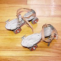 Pair of vintage Speed King adjustable roller skates on wooden floor, viewed from side angles showing leather straps and wheels.