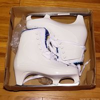 Top view of white women's figure ice skates with blades in original box, showing white laces and side embossed Lake Placid logo.