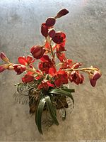 Top view of artificial floral arrangement showing red orchid-like flowers and green foliage in decorative pot