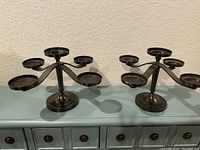 Two black metal candle stands with five candle holders each, arranged in a circular tiered design.
